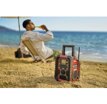 En Einhell byggnadsradio på stranden med en person i bakgrunden som njuter av en drink.