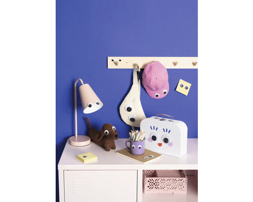 Dekorativa barnmöbler med lampa, pall, klädhängare, väska, keps, anteckningsblock, matlåda och pennor på byrå framför blå vägg