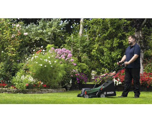 Man klipper gräs med en Bosch gräsklippare i en trädgård med blommor