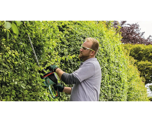 Man klipper häck med häcksax