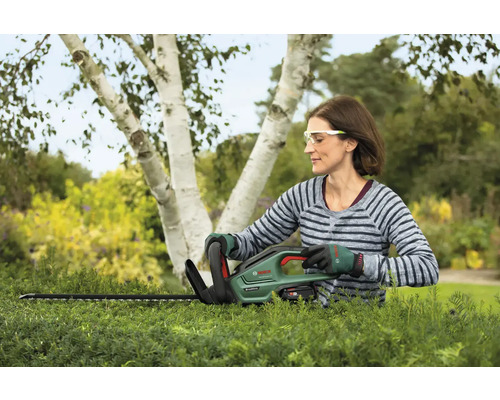 Kvinna klipper häck med en Bosch häcksax i trädgården.