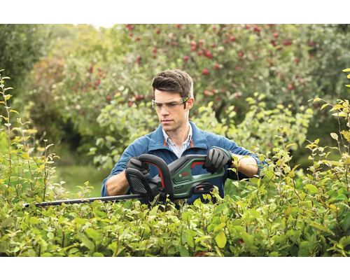 En man klipper en häck med en elektrisk häcksax från Bosch.