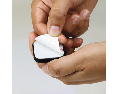 En hand drar av skyddsfilmen från en självhäftande möbelglidare.