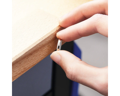 En person håller en tunn, rund metallbit mot en träkant.