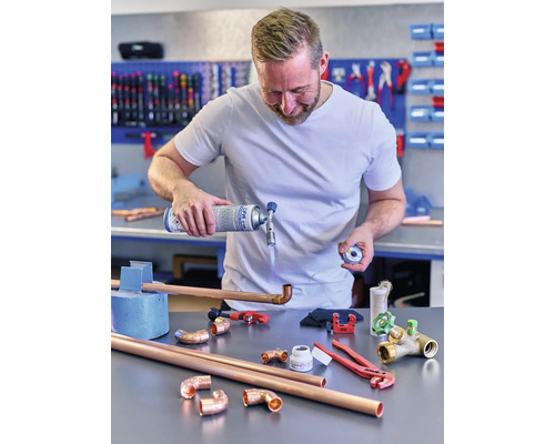 Man löder kopparrör med en gasbrännare och verktyg på ett bord.
