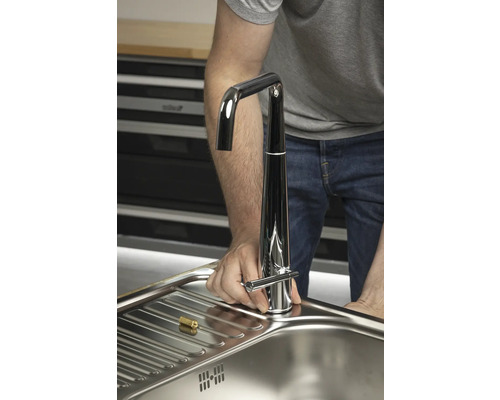 En man installerar en kran i en diskho.