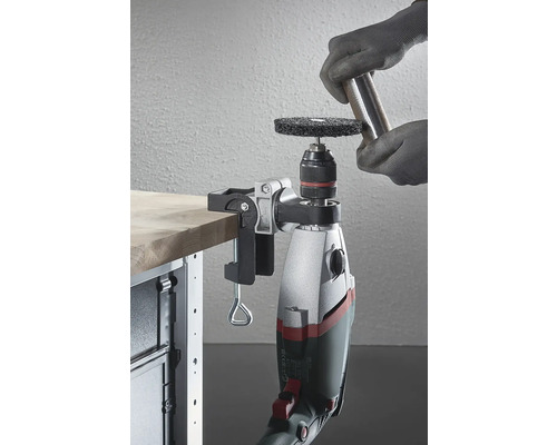 En borr med ett slipfäste, fäst vid en arbetsbänk, används för att bearbeta en bit metall.