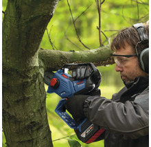 En man beskär en gren med en batteridriven motorsåg.