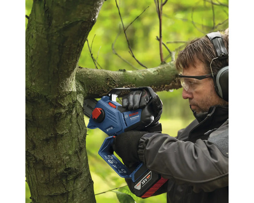 En man beskär en gren med en batteridriven motorsåg.