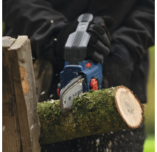 Person sågar vedträ med en Bosch batteridriven motorsåg
