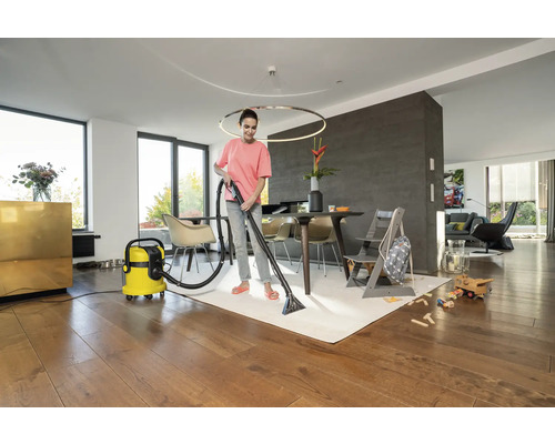 Kvinna rengör matta med en mattrengörare i ett vardagsrum