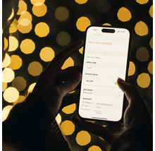 En person håller en smartphone med en app för schemaläggning av ett eluttag i handen.
