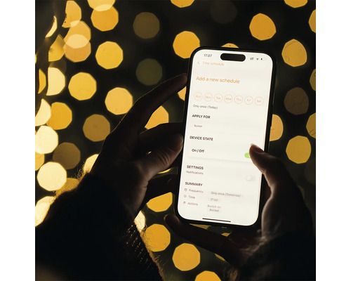 En person håller en smartphone med en app för schemaläggning av ett eluttag i handen.