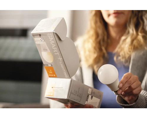 Kvinna håller SMART+ Lighting glödlampa med förpackning