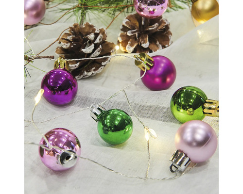 Dekorativa julgranskulor med tallkottar och ljusslinga på tyg