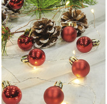 Dekorativt arrangemang med röda julgranskulor, ljusslinga, tallkottar och grangrenar.