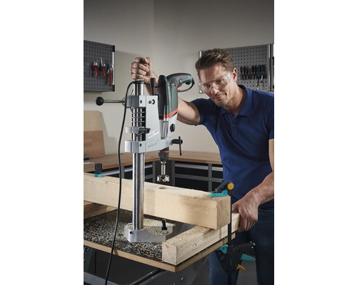 Man borrar ett hål i en träplanka med en borr och ett borrstativ.