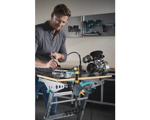 Man med skyddsglasögon bearbetar metalldel på en Wolfcraft arbetsbänk med ett multifunktionsverktyg.