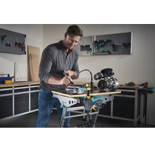 Man arbetar med ett multifunktionellt verktyg på ett arbetsstycke på en Wolfcraft arbetsbänk i en verkstad.