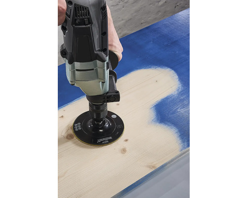 En person använder en slipmaskin för att ta bort färg från en träbräda.