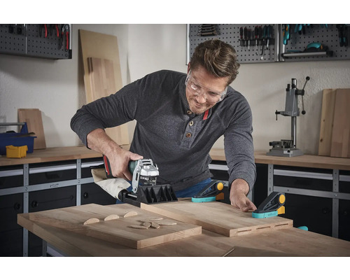 En man använder en spårfräs på träplankor i en verkstad.