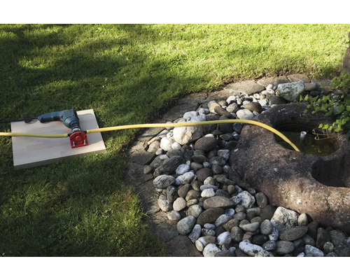 En borrmaskin med vattenanslutning och slang i trädgården.