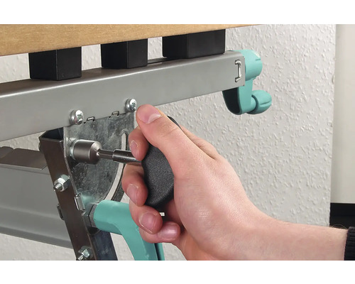 En person fäster en skruv med en skruvmejsel på en sängram i metall.