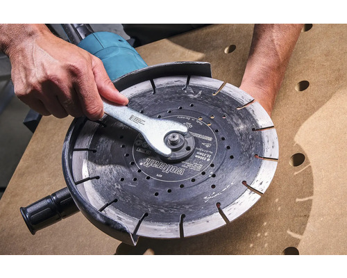 Person byter kapskiva med skiftnyckel på en vinkelslip