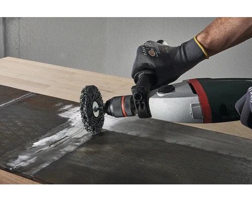 En stålborste används med en borrmaskin på en träplanka.