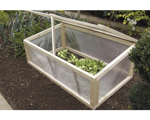 Drivbänk av trä och plast i en trädgårdsbädd med salladsplantor