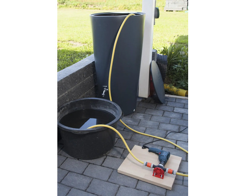 Regnvattentunna med kran, hink med vatten, borrmaskin och pump på stengolv