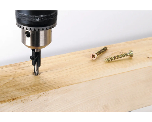 Borrmaskin borrar hål i träbräda bredvid två skruvar