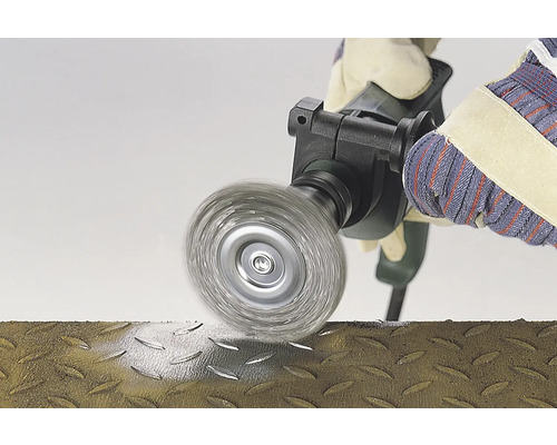 Stålborste i bruk på en metallyta, hanterad av en person med handskar.