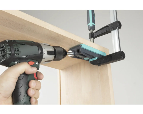 Sladdlös skruvdragare som borrar genom en borrguide i en träplanka