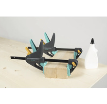 Två enhandsspännare från Wolfcraft fixerar träbitar på en arbetsbänk, en flaska lim står bredvid.