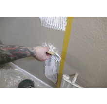 En person applicerar kakelfix på en vägg med en spackel.