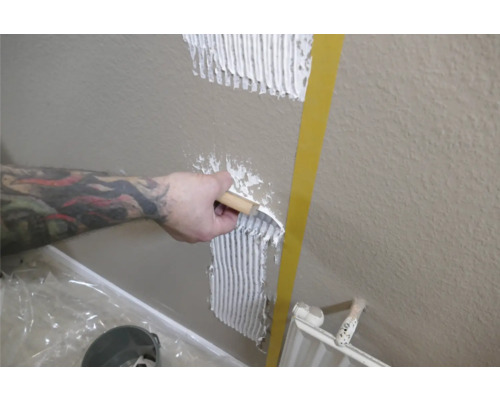 En person applicerar kakelfix på en vägg med en spackel.