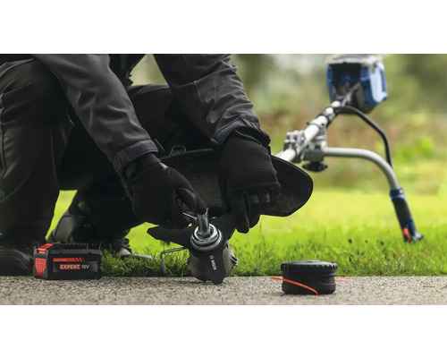 En person byter blad på en grästrimmer med ett batteri och en spole i närheten.