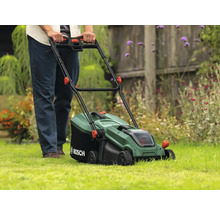 En person använder en grön Bosch gräsklippare på en gräsmatta.