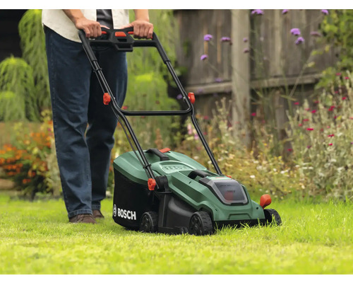 En person använder en grön Bosch gräsklippare på en gräsmatta.