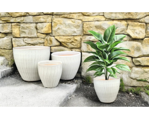 Grupp av blomkrukor med räfflad yta och en krukväxt mot en stenmur