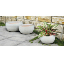 Tre runda blomkrukor utomhus framför en stenmur.