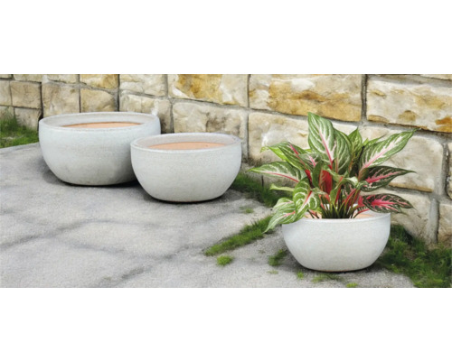 Tre runda blomkrukor utomhus framför en stenmur.