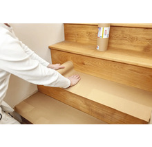 En person täcker en trätrappa med skyddspapper.