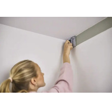 Kvinna målar vägg med färgroller i ett hörn.