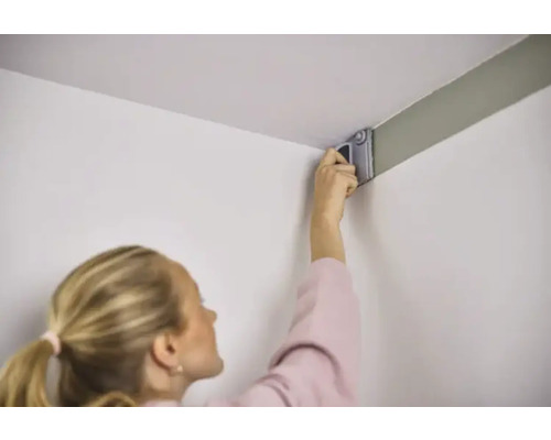 Kvinna målar vägg med färgroller i ett hörn.