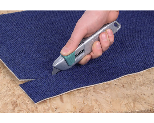 En hand skär en matta med en mattkniv.