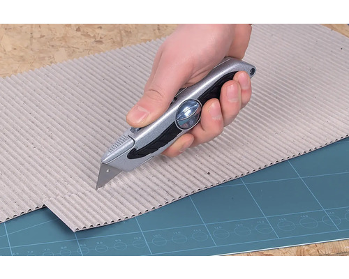 En hand skär kartong med en universalkniv.