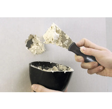 Ett hål i en vägg repareras med en spackel och fyllmedel.