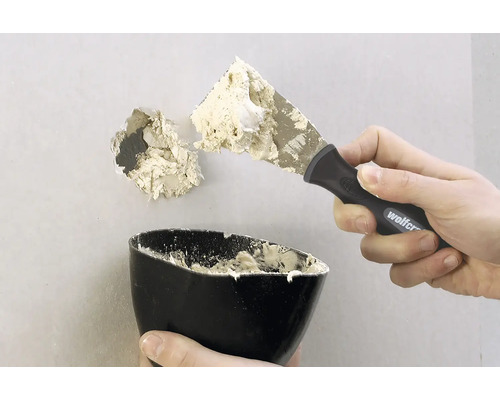 Ett hål i en vägg repareras med en spackel och fyllmedel.